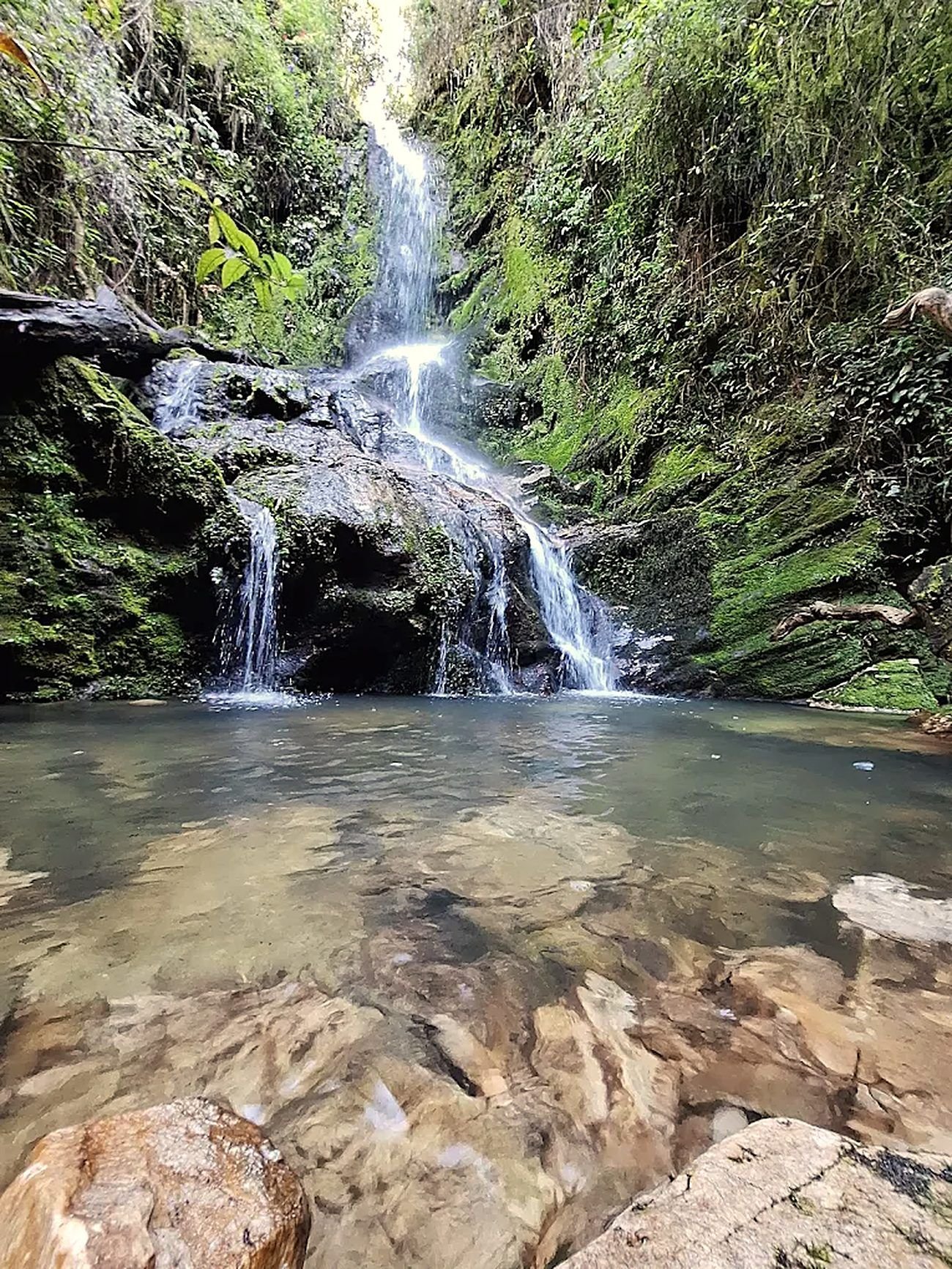 Cachoeira entre pedras cobertas de musgo, com poço de água transparente